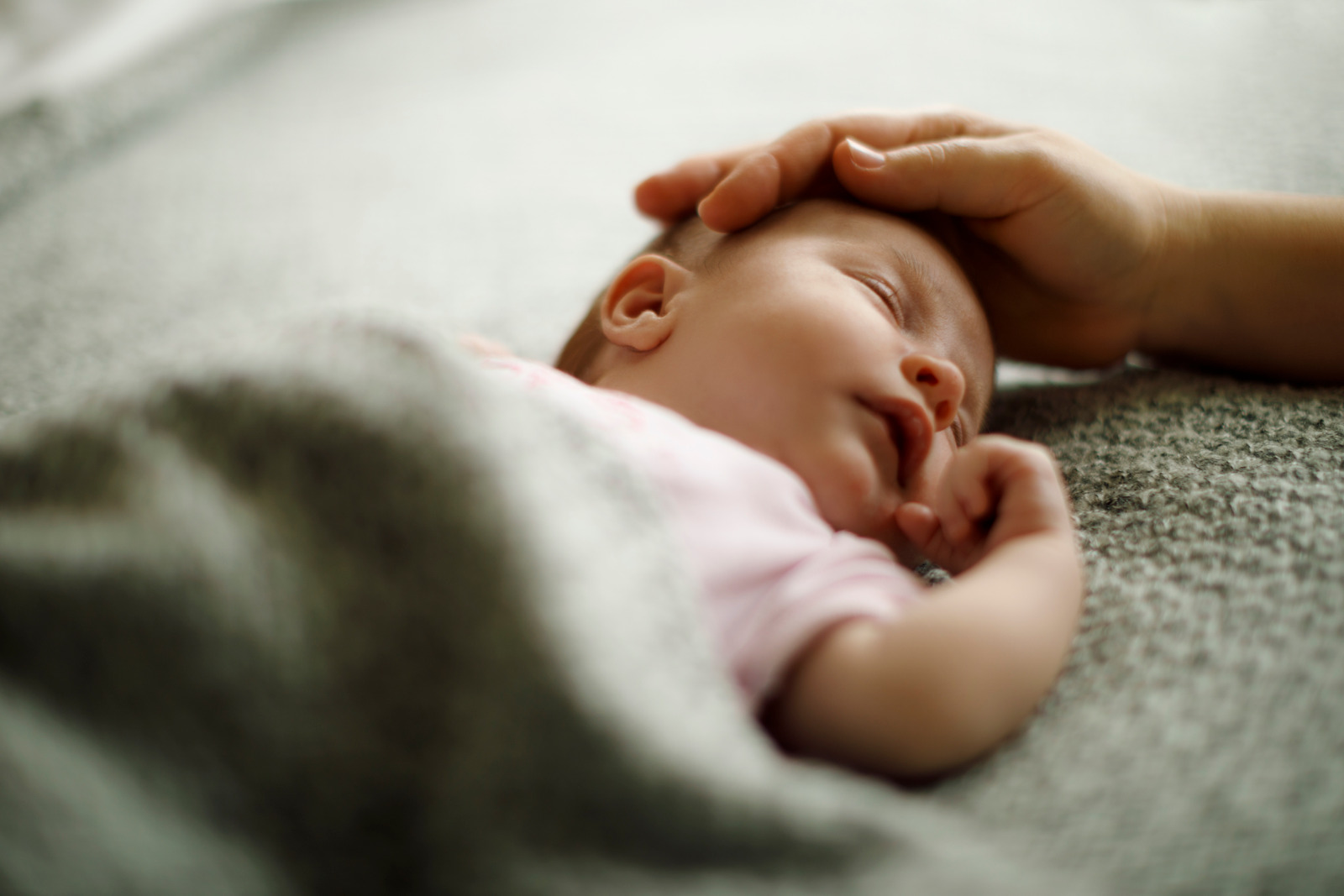 A sleeping newborn resting beside a parent's hand